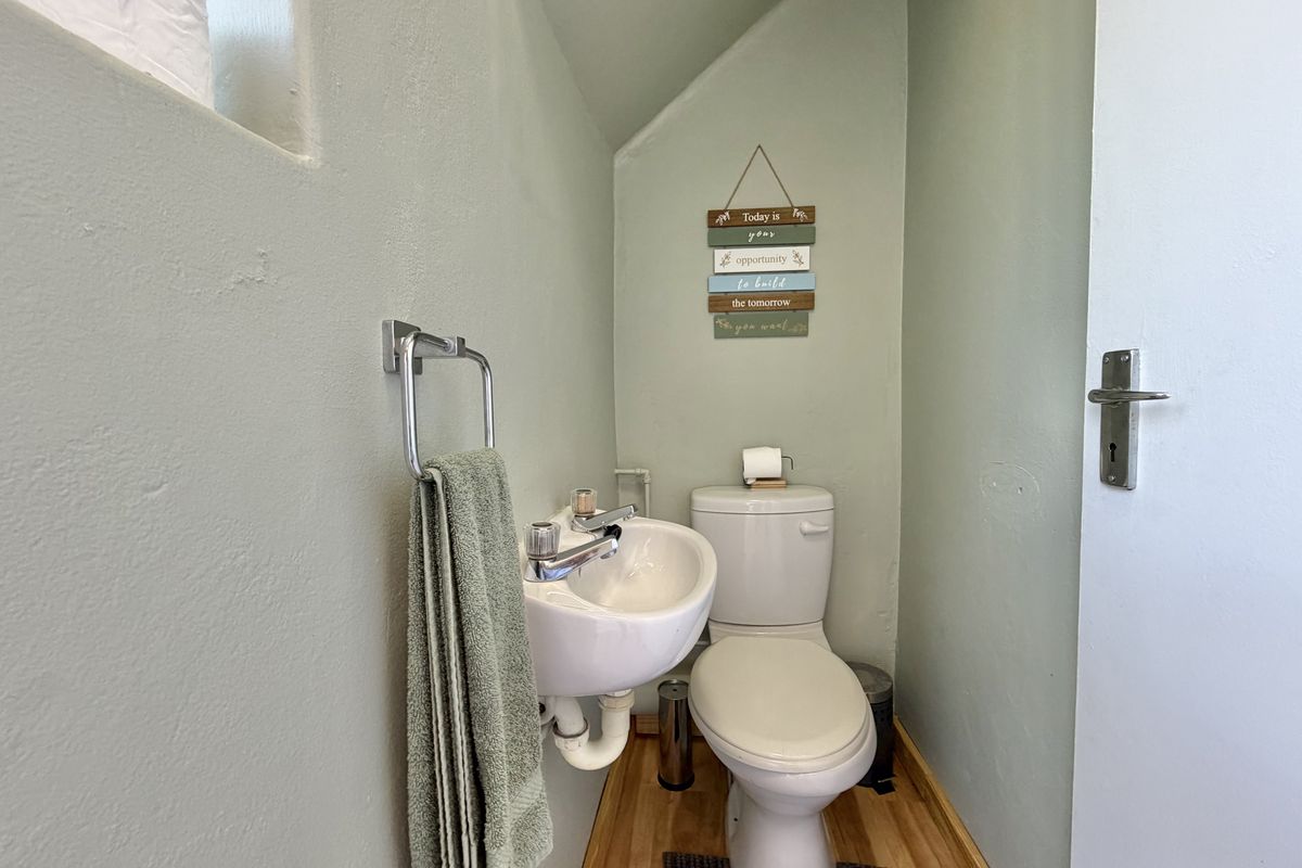 A compact guest bathroom featuring a wall-mounted basin, standard toilet, and laminate flooring with neutral wall tones.
