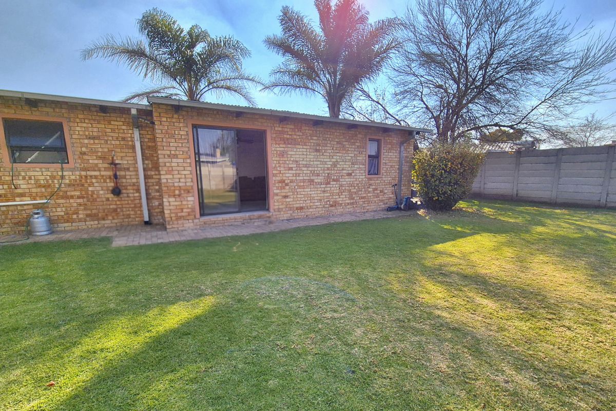 Rear view of the house featuring a brick facade, sliding glass door access, and a spacious private garden area.