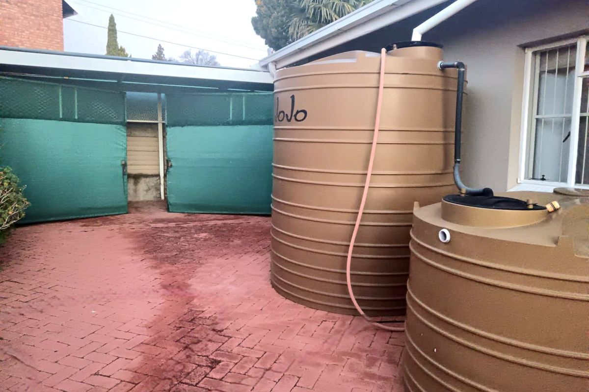 Exterior rear area featuring two large water storage tanks connected to the roof gutter system and paved ground surface.