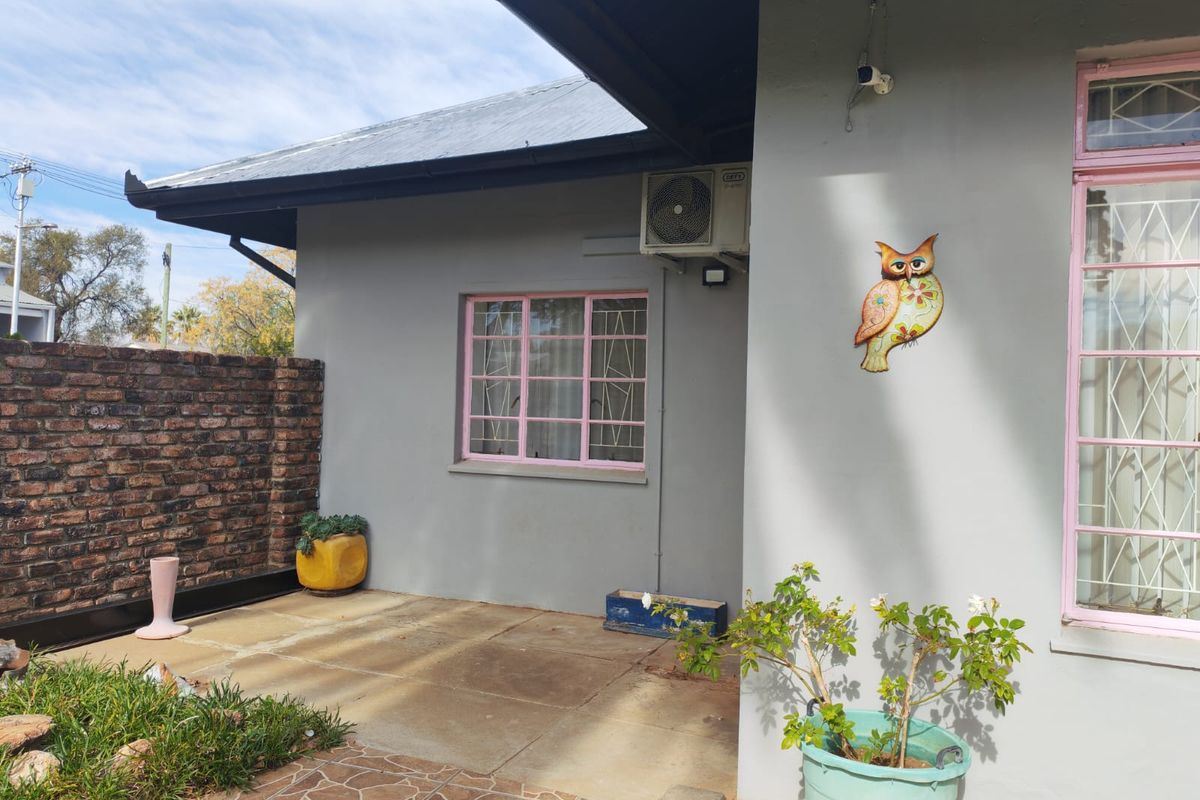 A paved rear patio area featuring a brick boundary wall, exterior air conditioning unit, and security bars on the windows.