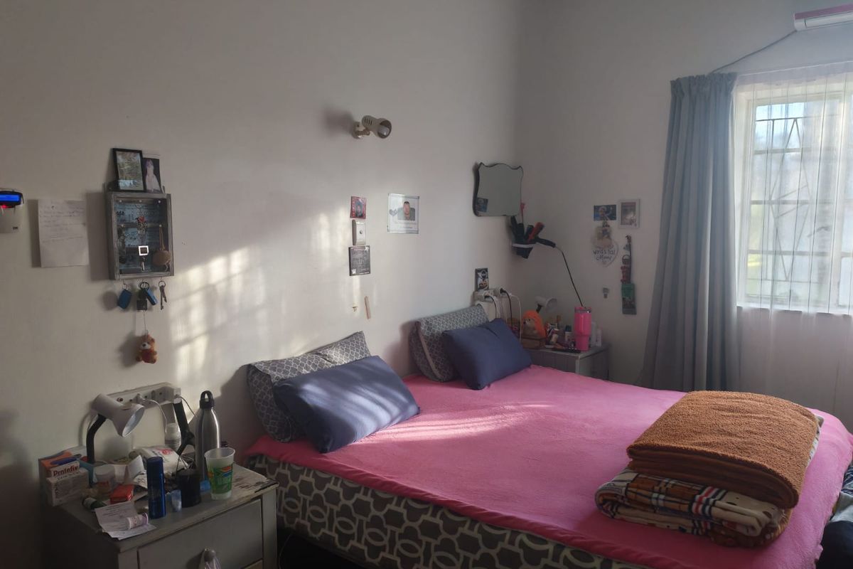 A functional bedroom featuring a window with security bars, wall-mounted lighting, and an integrated air conditioning unit.