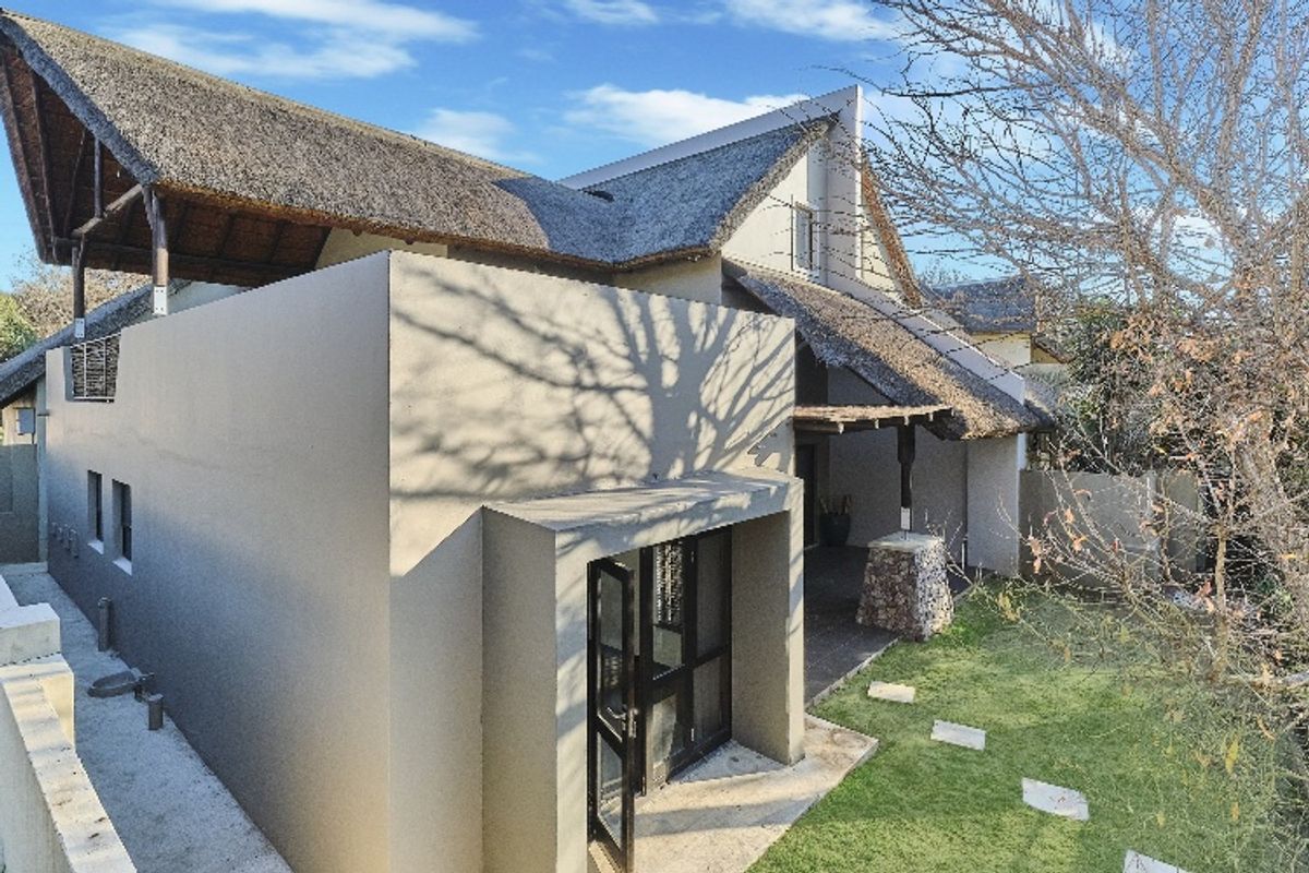Exterior view of a townhouse featuring a distinctive thatched roof, modern rendered walls, and a small private garden area with paved stepping stones.