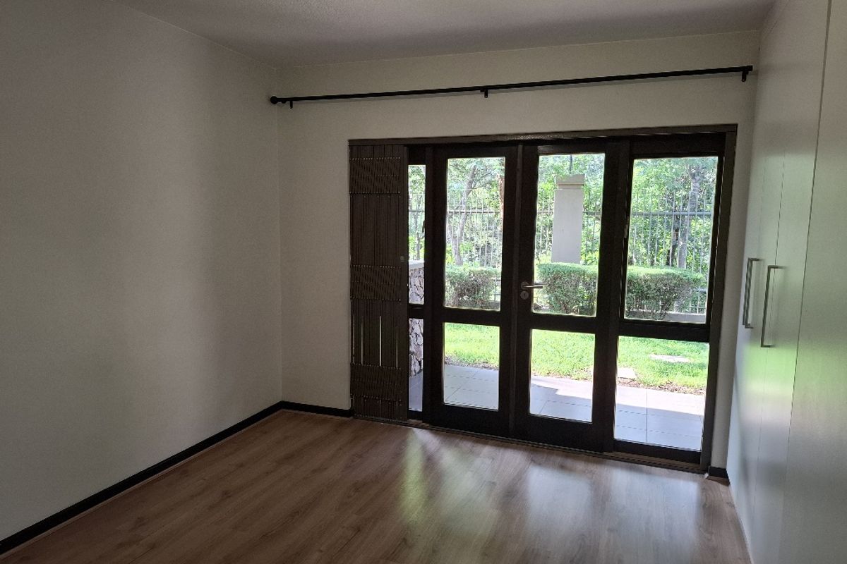 A bright bedroom featuring laminate flooring, built-in cupboards, and large glass sliding doors providing direct access to the garden.