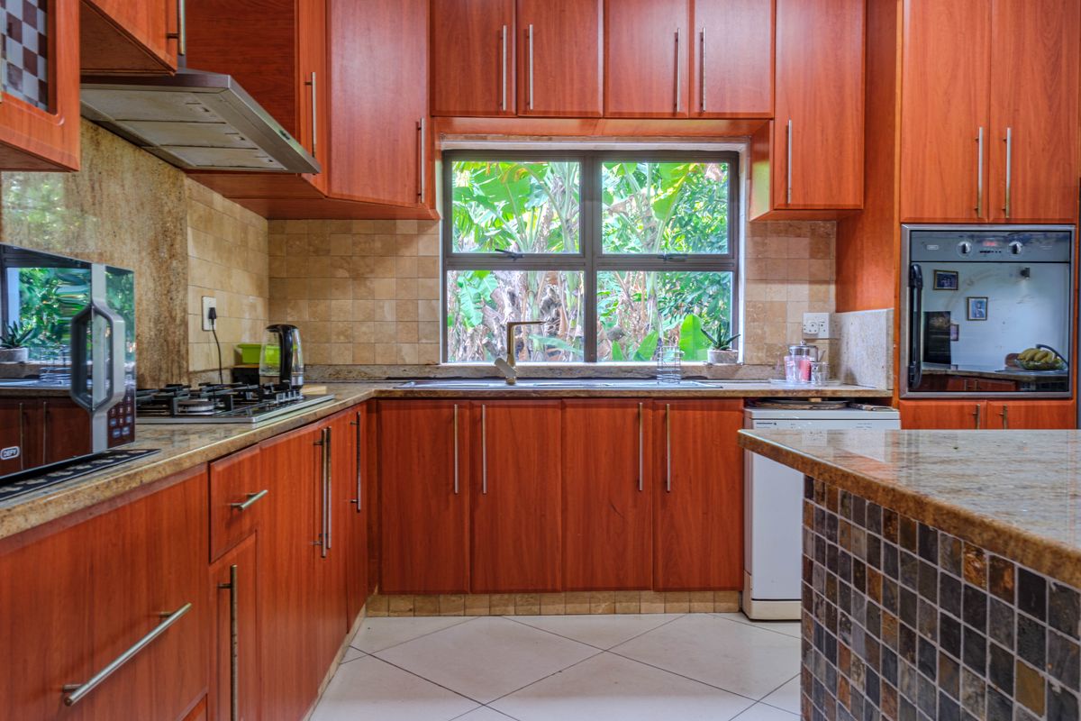A functional kitchen featuring warm-toned wooden cabinetry, granite countertops, a built-in oven, gas hob, and a tiled backsplash with a garden-facing window.