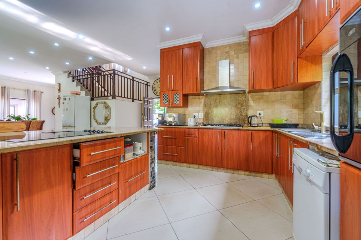 Spacious kitchen featuring warm-toned wooden cabinetry, granite countertops, a built-in gas hob with extractor fan, and tiled flooring, seamlessly flowing into the living area.