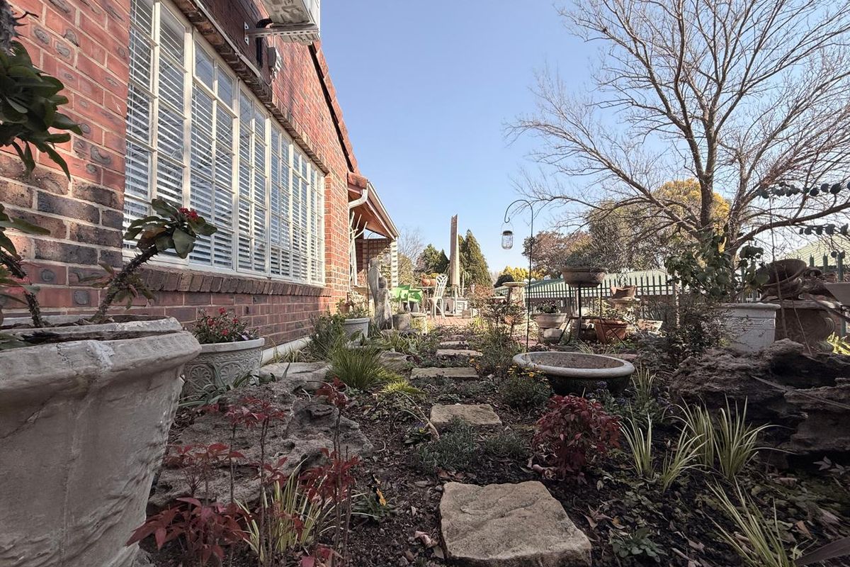 A view of the rear garden area featuring a brick exterior wall, stone pathway, and established landscaping along the side of the townhouse.
