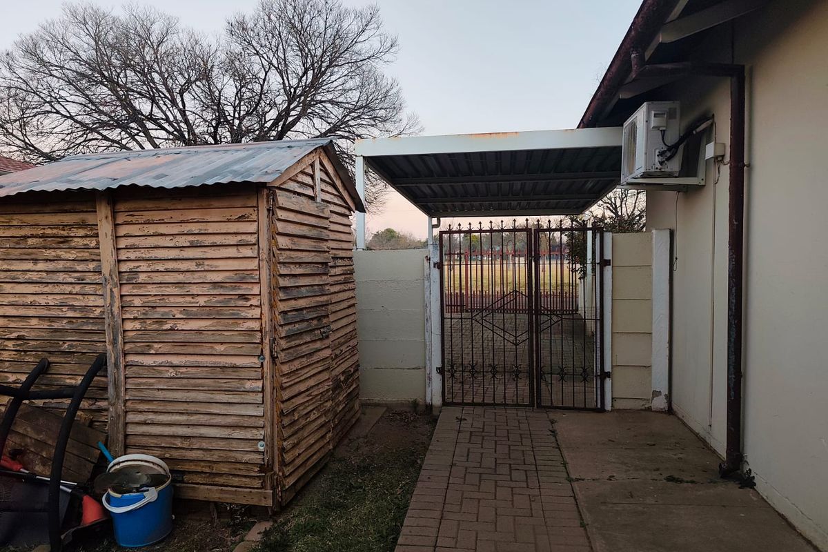 Exterior view of the property featuring a paved walkway, a metal carport, and a weathered timber storage shed.