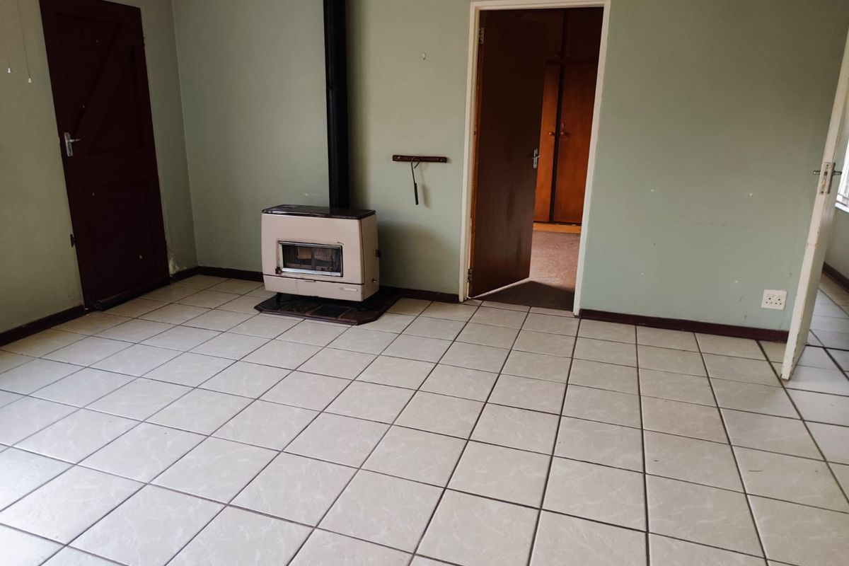 A spacious living room featuring light-colored floor tiles, a built-in fireplace, and direct access to an adjacent room.