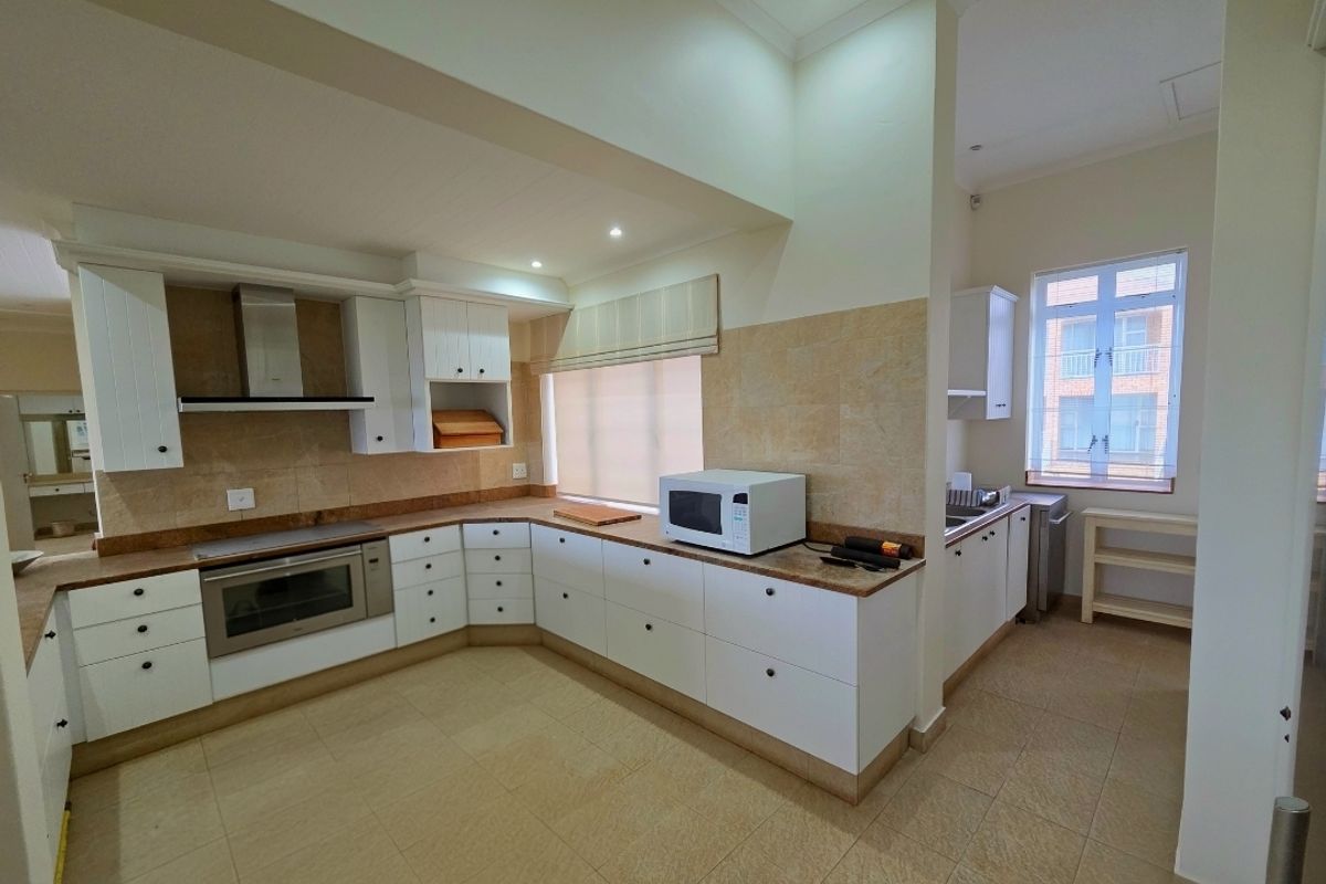 A functional kitchen featuring white cabinetry, stone countertops, a built-in oven, extractor fan, and a separate scullery area with a sink.