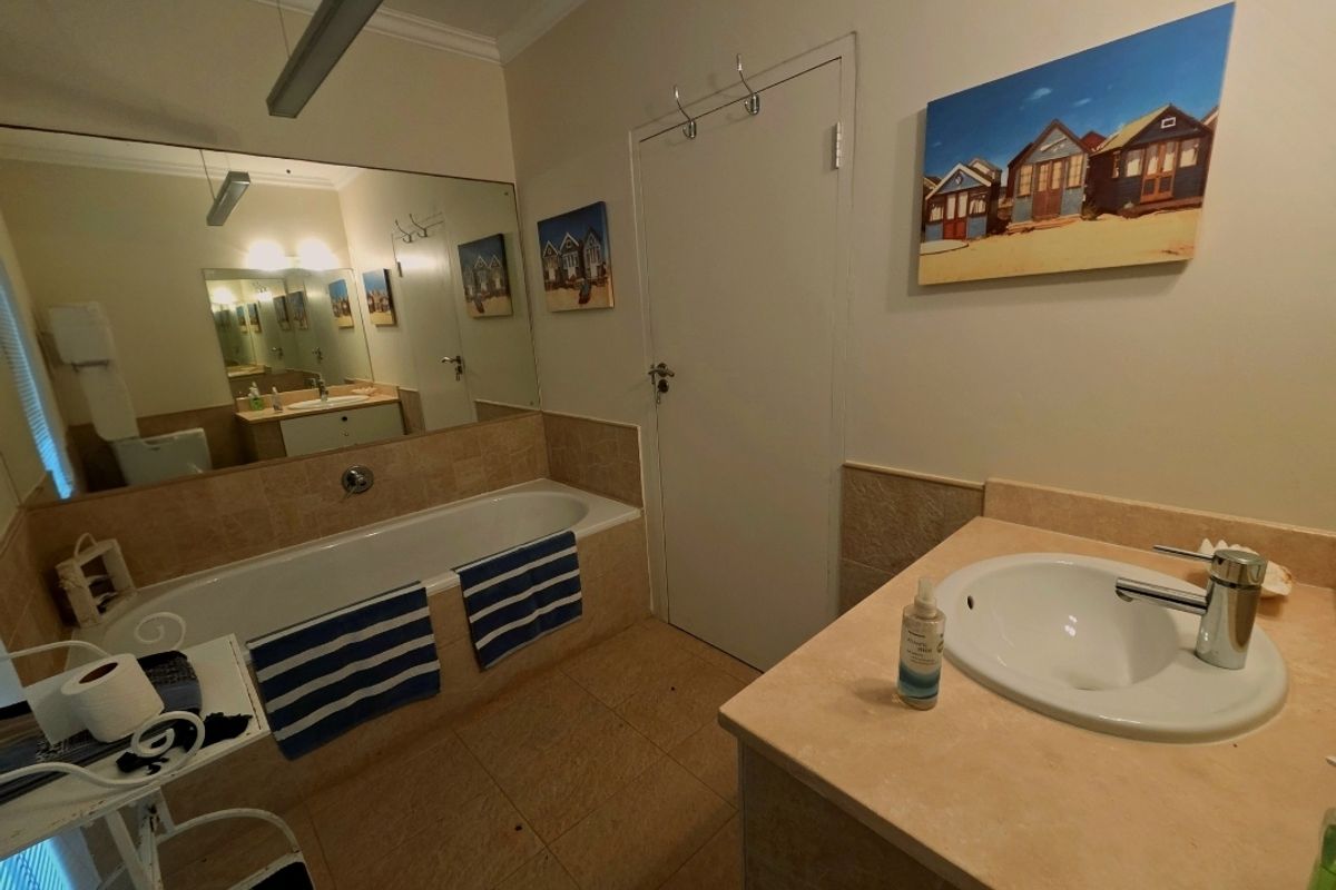 A functional bathroom featuring a built-in bathtub with tiled surround, a large wall-mounted mirror, and a single vanity basin with stone countertop.