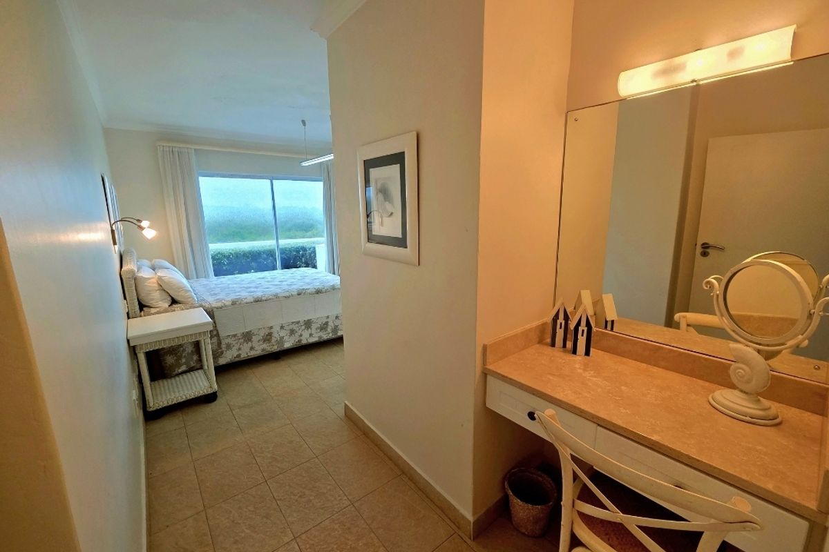 A bedroom featuring a built-in vanity area with a large mirror and integrated lighting, leading into the sleeping space with tiled flooring.