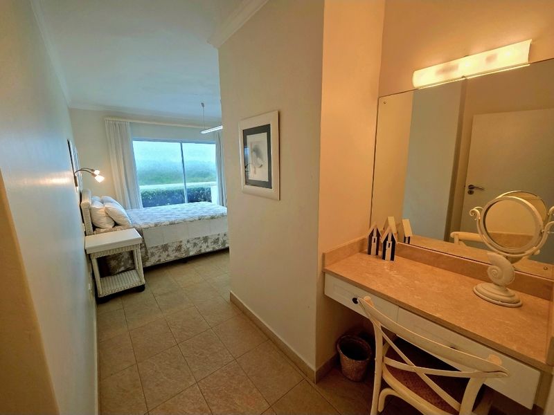 A bedroom featuring a built-in vanity area with a large mirror and integrated lighting, leading into the sleeping space with tiled flooring.