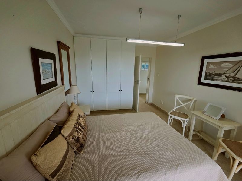 A well-lit bedroom featuring built-in floor-to-ceiling wardrobes, neutral wall finishes, and tiled flooring, providing a functional and comfortable living space.
