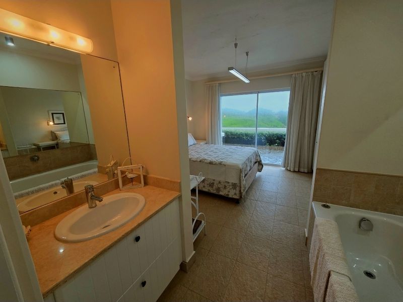An open-plan bedroom suite featuring an integrated bathroom with a vanity, basin, and bathtub, leading out to a private balcony with scenic views.