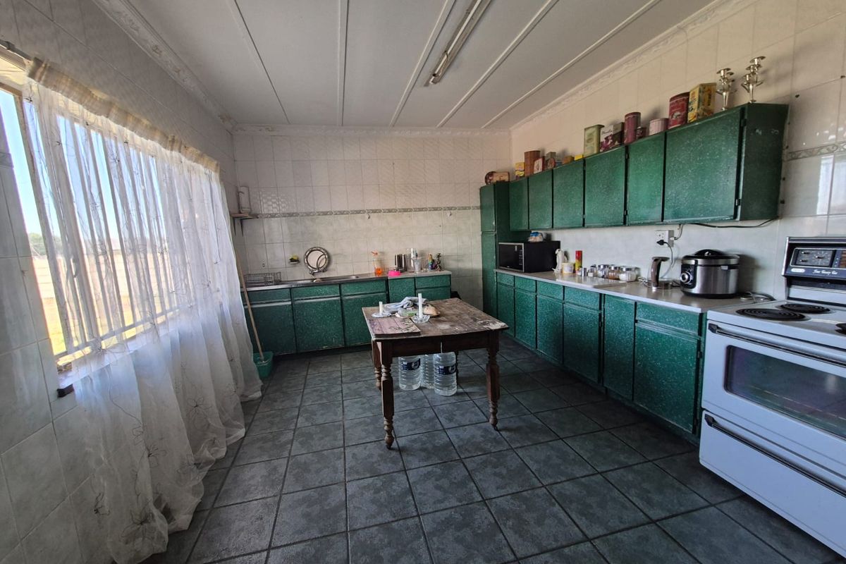 A spacious kitchen featuring dated green cabinetry, tiled flooring, and wall-to-wall tiling, offering a functional layout with ample storage space.