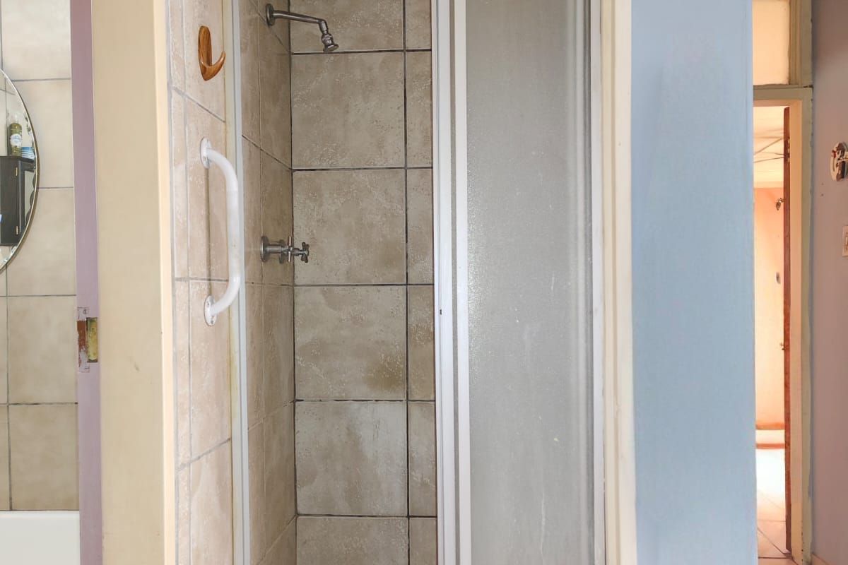 A functional shower cubicle featuring tiled walls, a grab rail, and a sliding glass door, situated within a bathroom space.