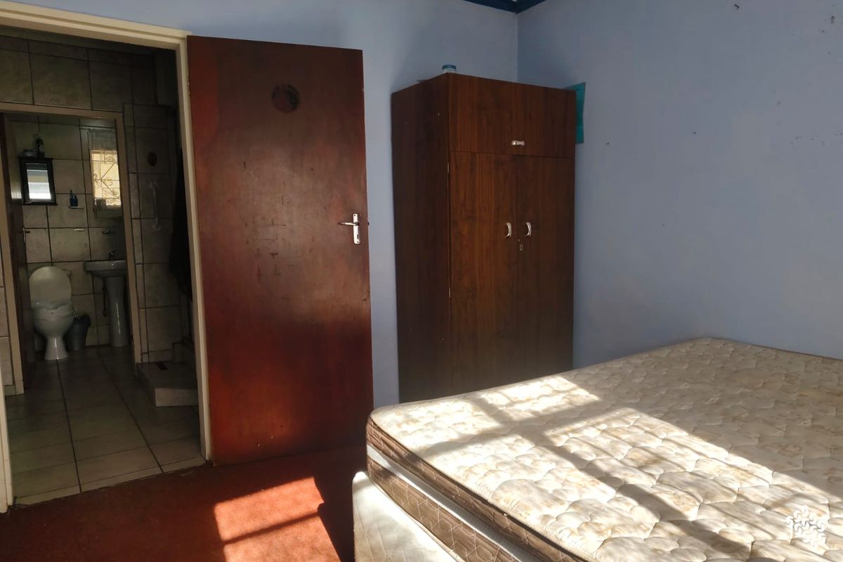A bedroom featuring an en-suite bathroom with tiled flooring and basic fixtures, offering a functional layout with potential for cosmetic updates.