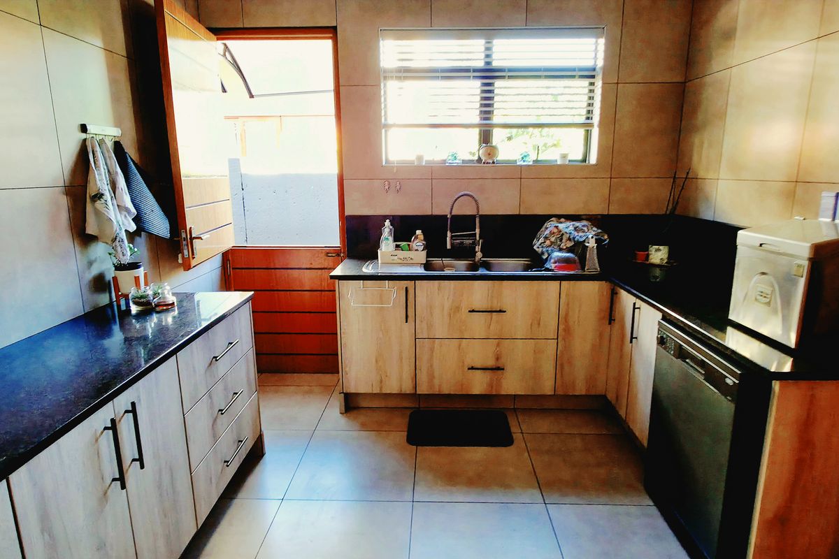 A functional kitchen featuring light wood-grain cabinetry, dark granite countertops, tiled walls, and a stainless steel sink with a modern mixer tap.