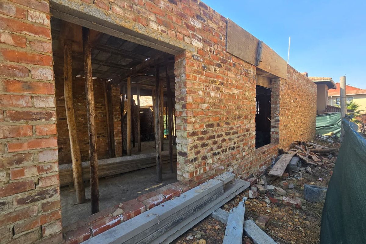 A view of a residential property under construction, featuring exposed brick walls and temporary structural supports on a vacant land site.
