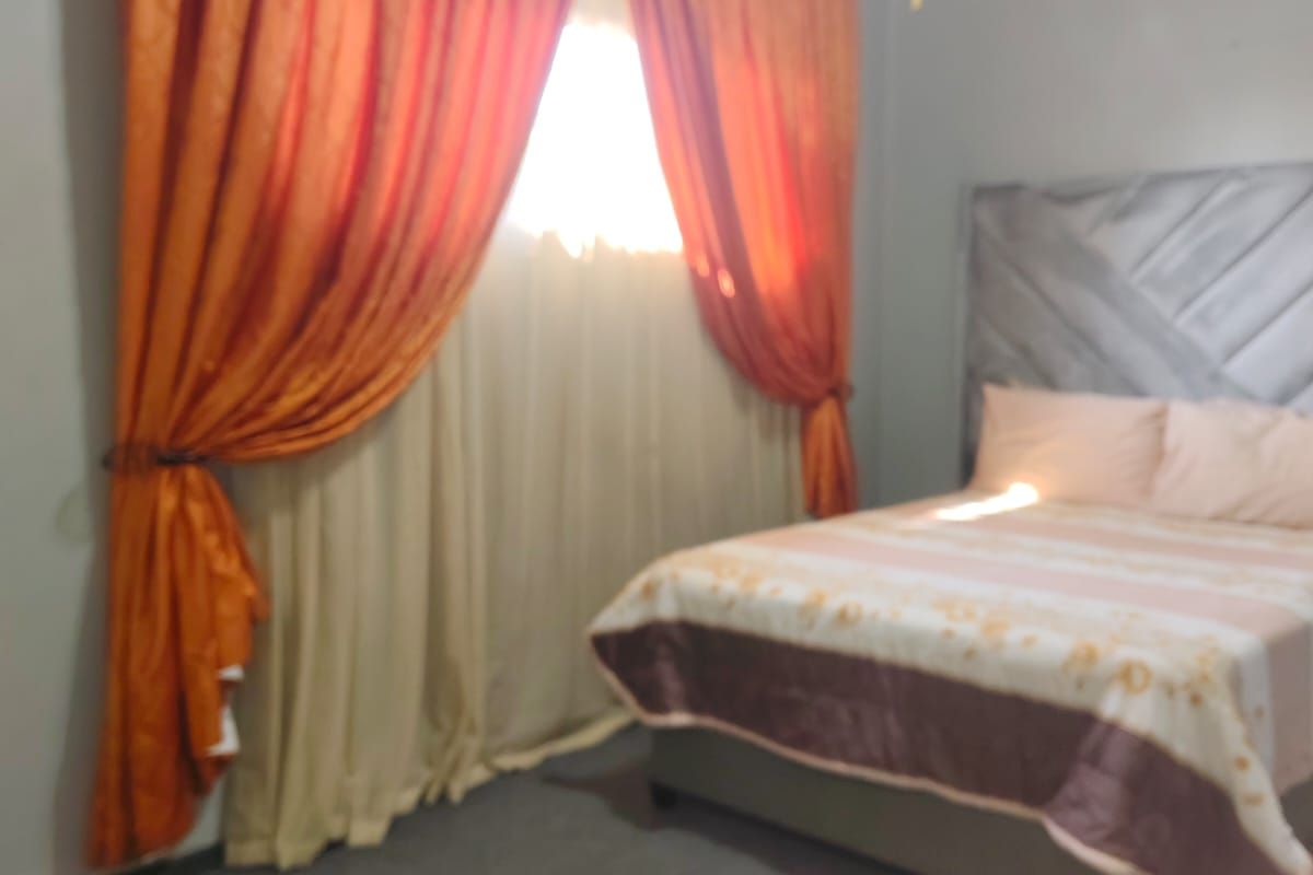 A bedroom featuring carpeted flooring, a ceiling fan, and a window dressed with curtains.