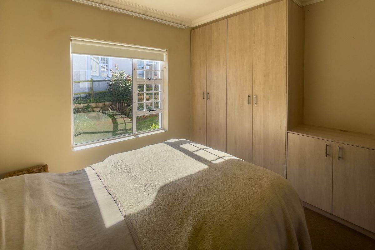 A bedroom featuring built-in light wood cabinetry and a window overlooking the garden.