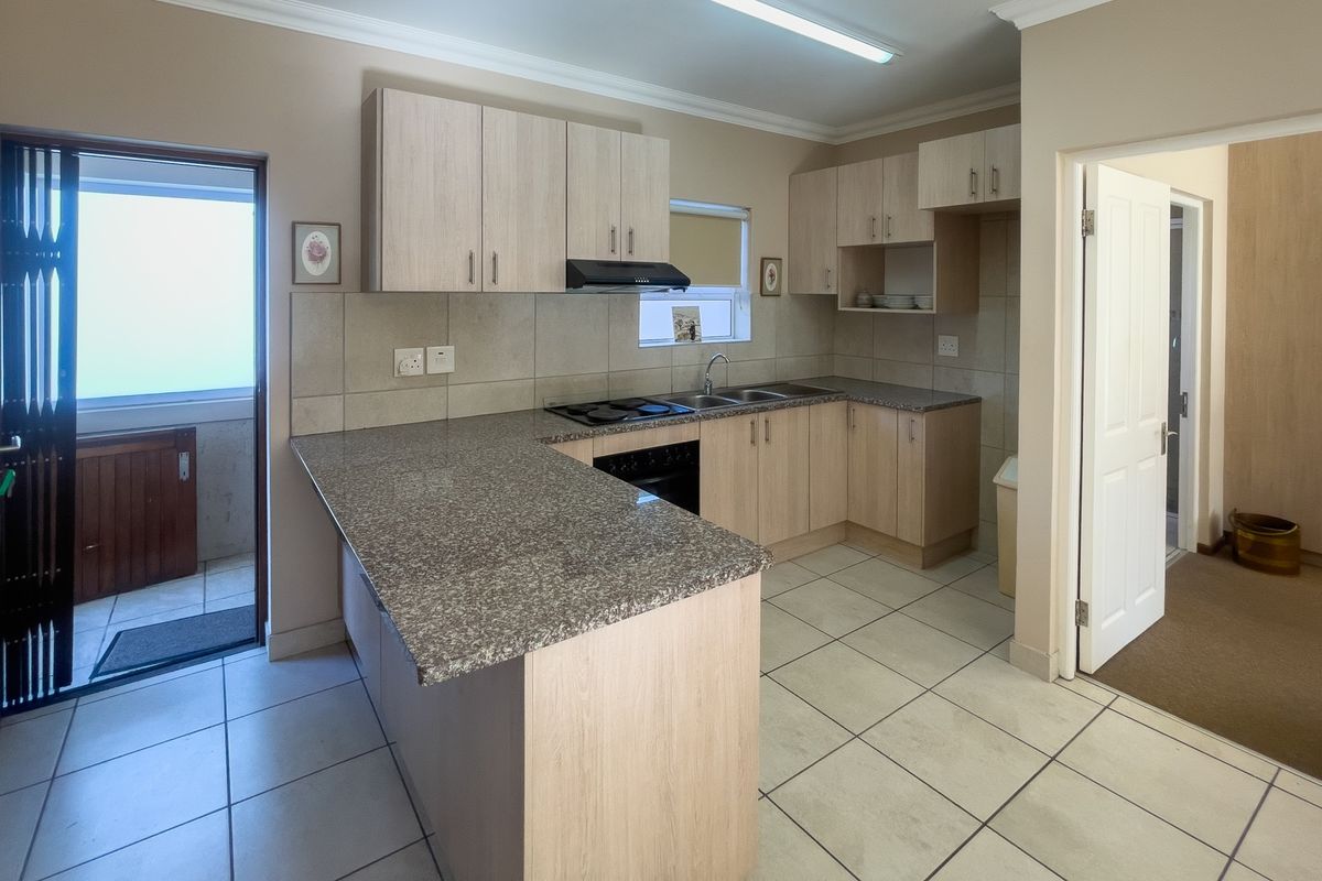 A functional kitchen featuring light wood cabinetry, granite countertops, a built-in oven and hob, and tiled flooring with direct access to an outdoor area.