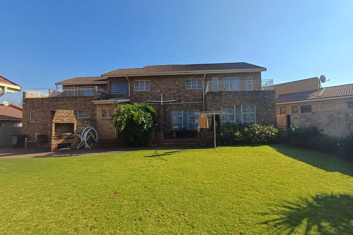 Rear view of a double-story brick house featuring a spacious lawn, a built-in braai area, and upper-level balconies.