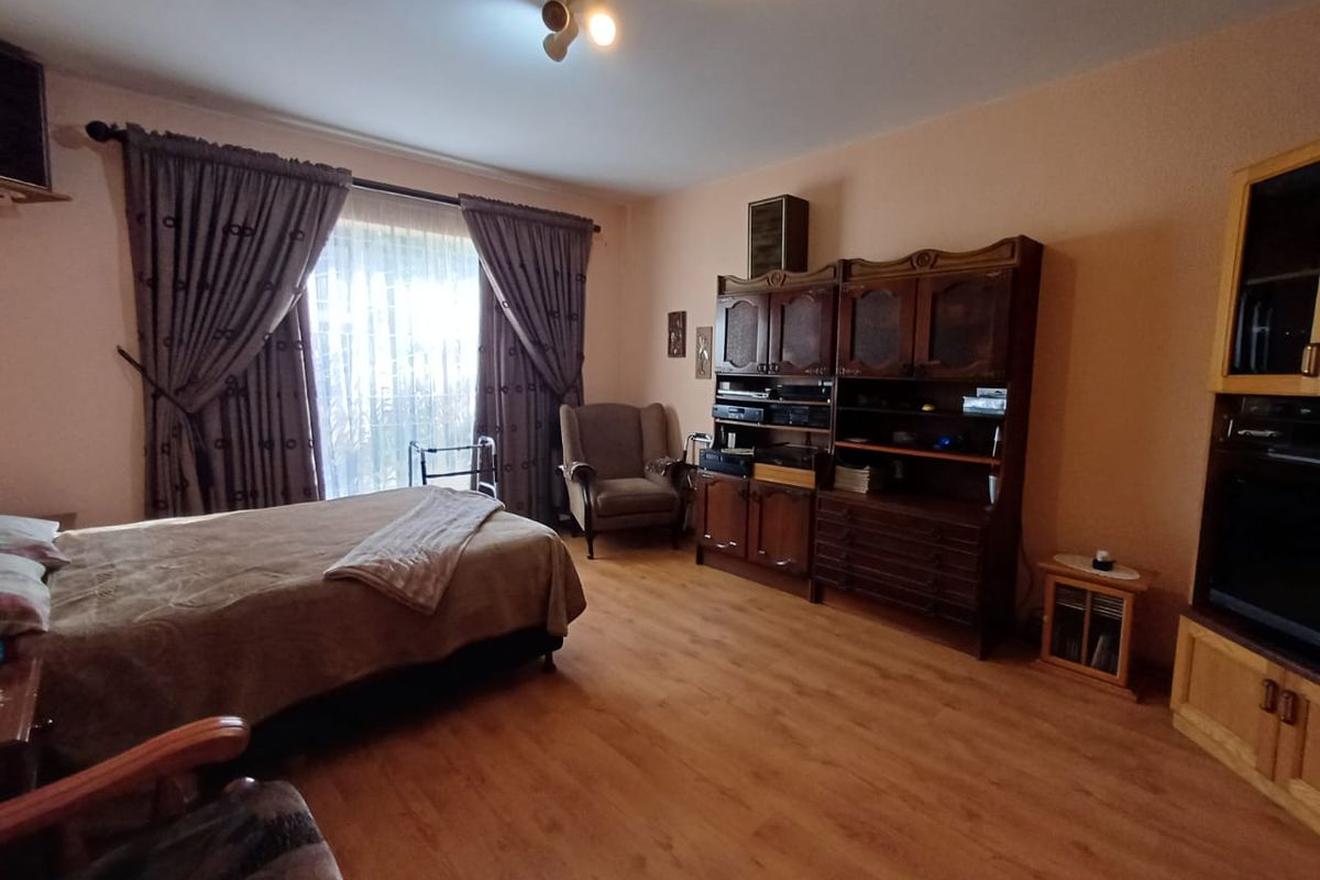 A bedroom featuring laminate flooring and a large window with curtains, providing a functional living space.