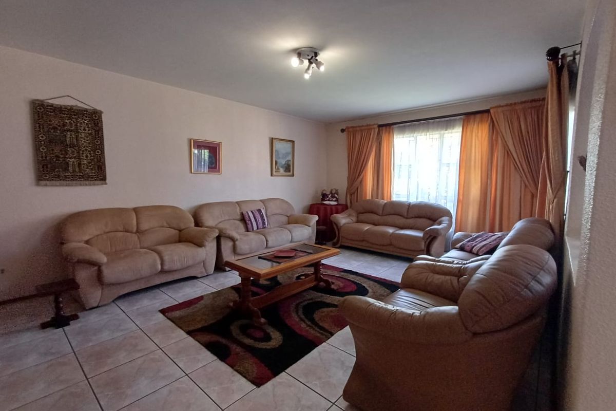 A spacious living room featuring neutral tiled flooring and large windows with curtain rails, providing a functional and comfortable family living space.