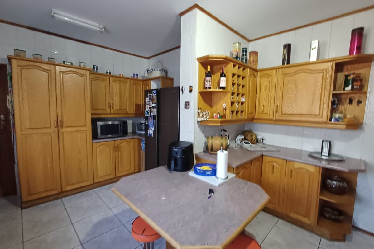 A functional kitchen featuring traditional wooden cabinetry, tiled backsplash, and a central breakfast nook with laminate countertops and tiled flooring.