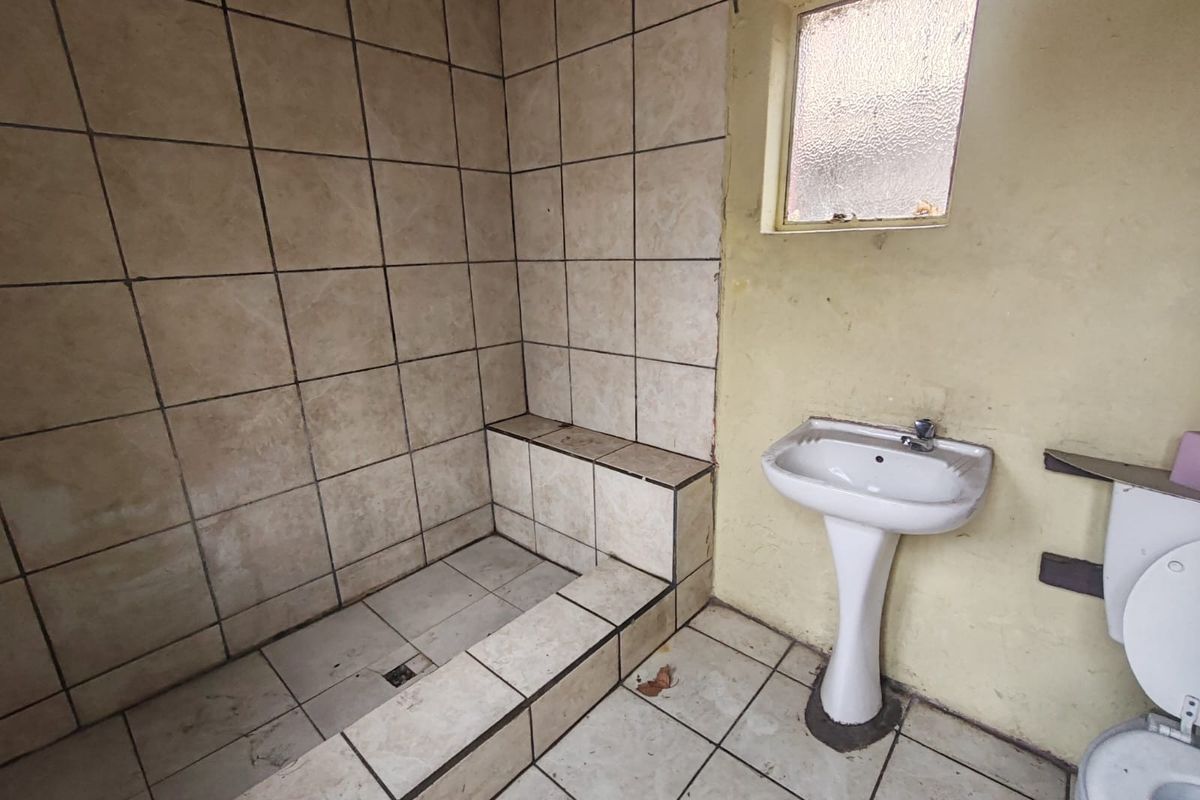 A dated bathroom featuring a tiled shower enclosure, pedestal basin, and toilet, requiring significant renovation and cosmetic updates to restore functionality and appeal.