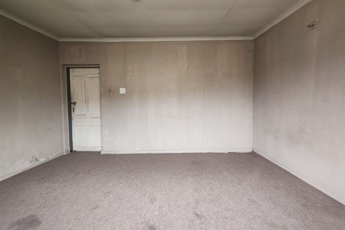 An empty, dated living room featuring worn carpeting and plain walls, offering a blank canvas for renovation and modernization.