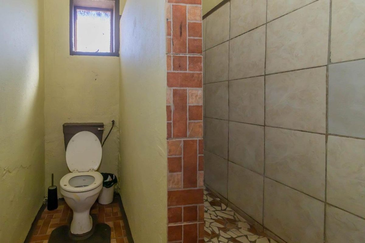 A dated bathroom featuring a toilet and a tiled shower area with a brick-accented partition wall.