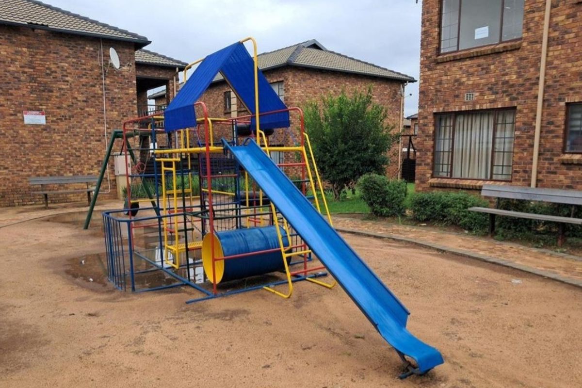 Communal outdoor area featuring a playground structure with a slide, set within a brick apartment complex courtyard.