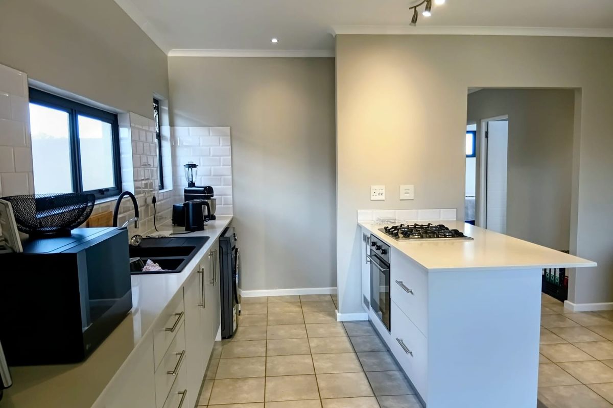 Modern kitchen featuring a central island with built-in gas hob and oven, sleek cabinetry, subway tile backsplash, and tiled flooring.