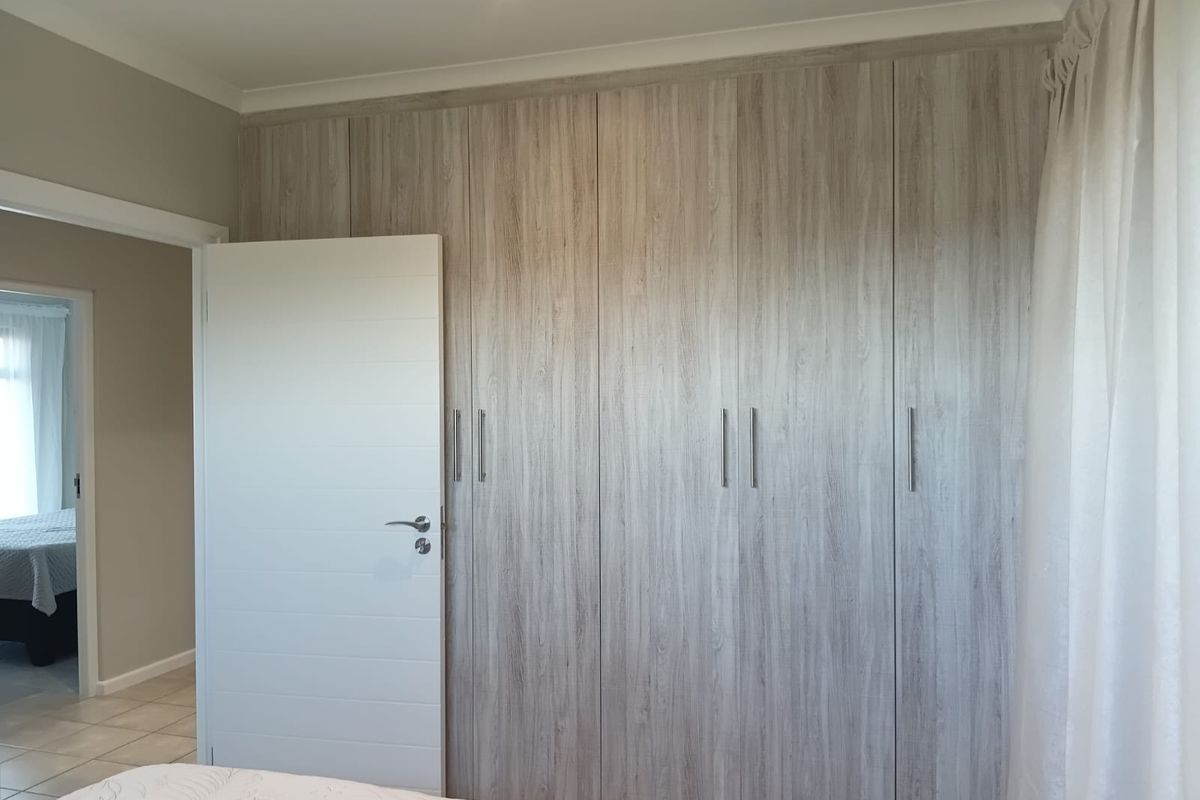 A bedroom featuring floor-to-ceiling built-in cupboards with a modern wood-grain finish and a clean, neutral interior design.