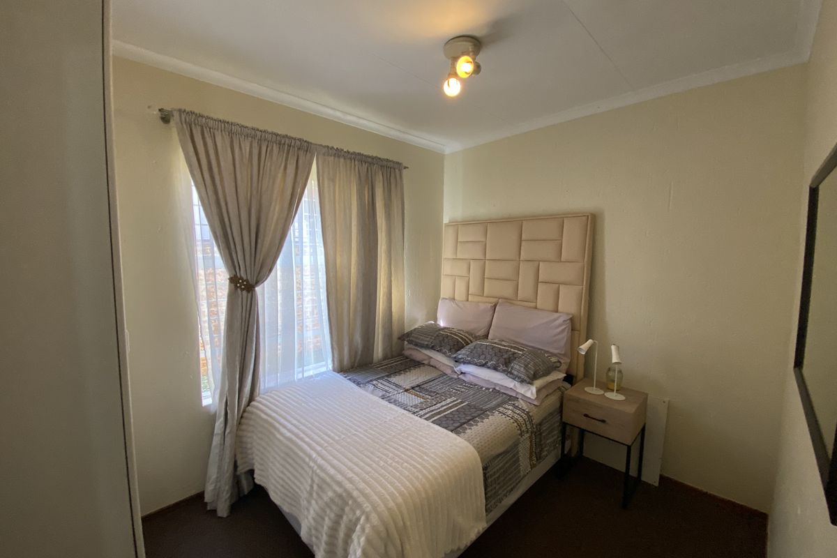 A compact bedroom featuring neutral wall finishes, a window with curtain tracks, and a ceiling-mounted light fixture.
