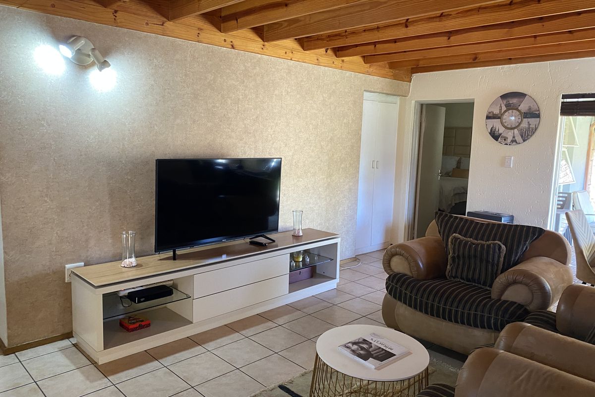 A living room featuring exposed timber ceiling beams, tiled flooring, and a neutral wall finish, providing a cozy and functional living space.