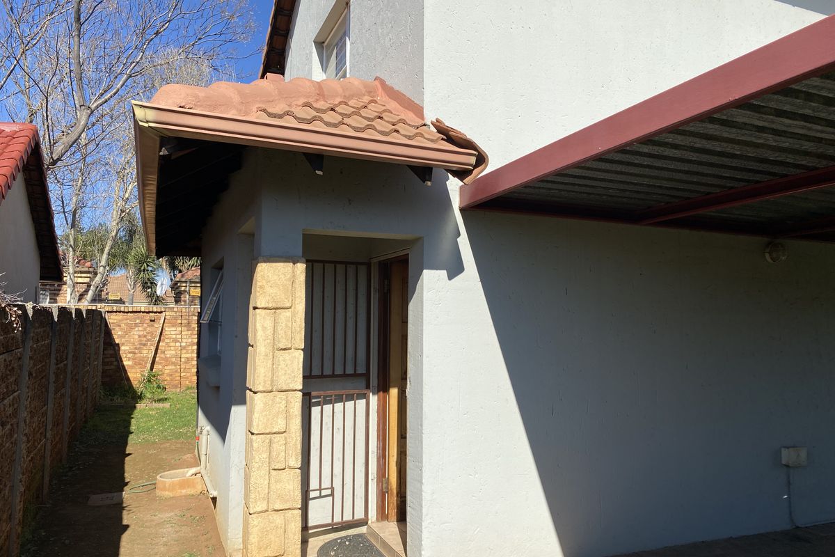 Side view of the property featuring a covered carport area, stone-clad pillar, and a secure entrance door with a security gate.