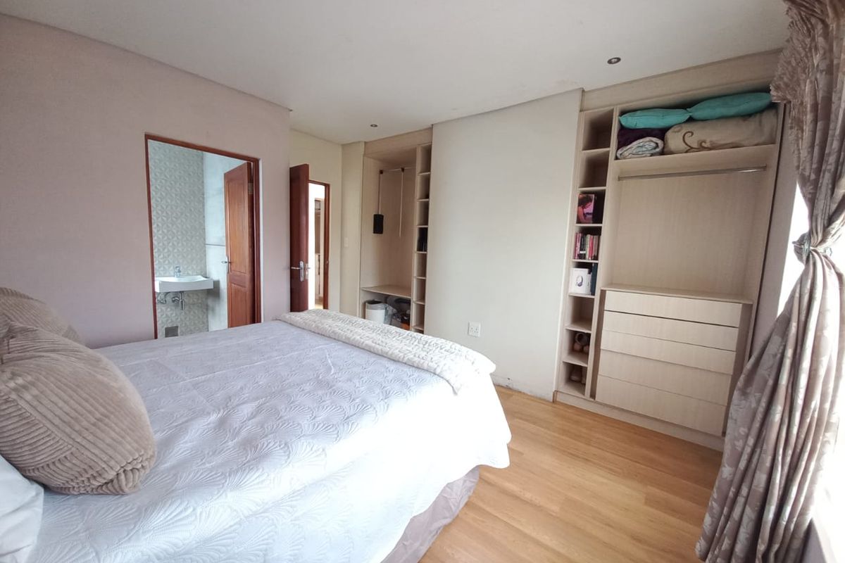 A bedroom featuring built-in wooden cabinetry and shelving, with an adjoining en-suite bathroom visible through the doorway.
