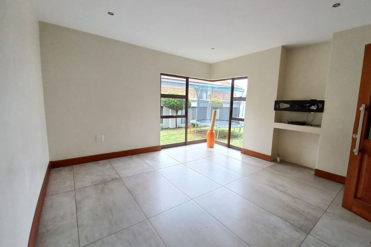 A bright, empty living room featuring large corner windows, neutral tiled flooring, and a built-in wall niche for media equipment.