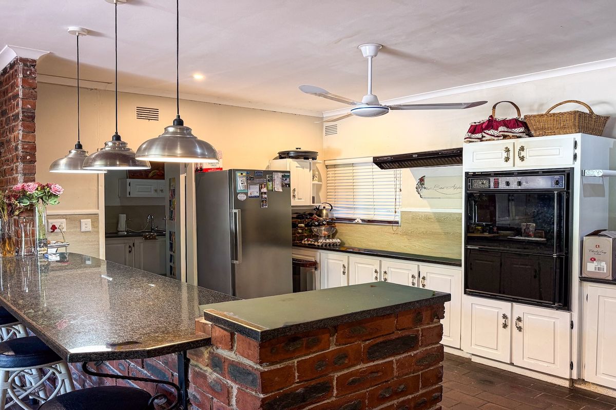 A spacious kitchen featuring a large granite-topped breakfast bar, built-in oven, extractor fan, and ample cabinetry, with an adjacent scullery area.