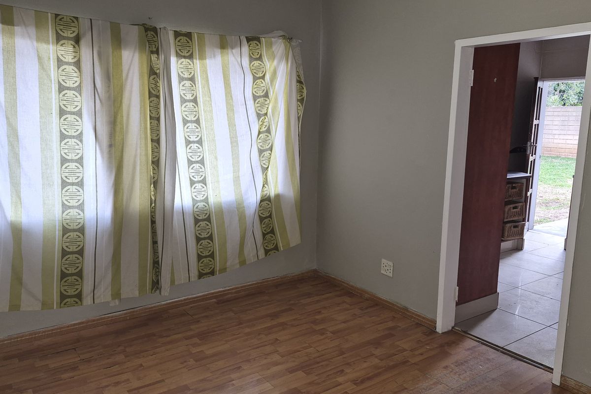 A bedroom featuring laminate flooring and a doorway leading to an adjacent tiled area with garden access.
