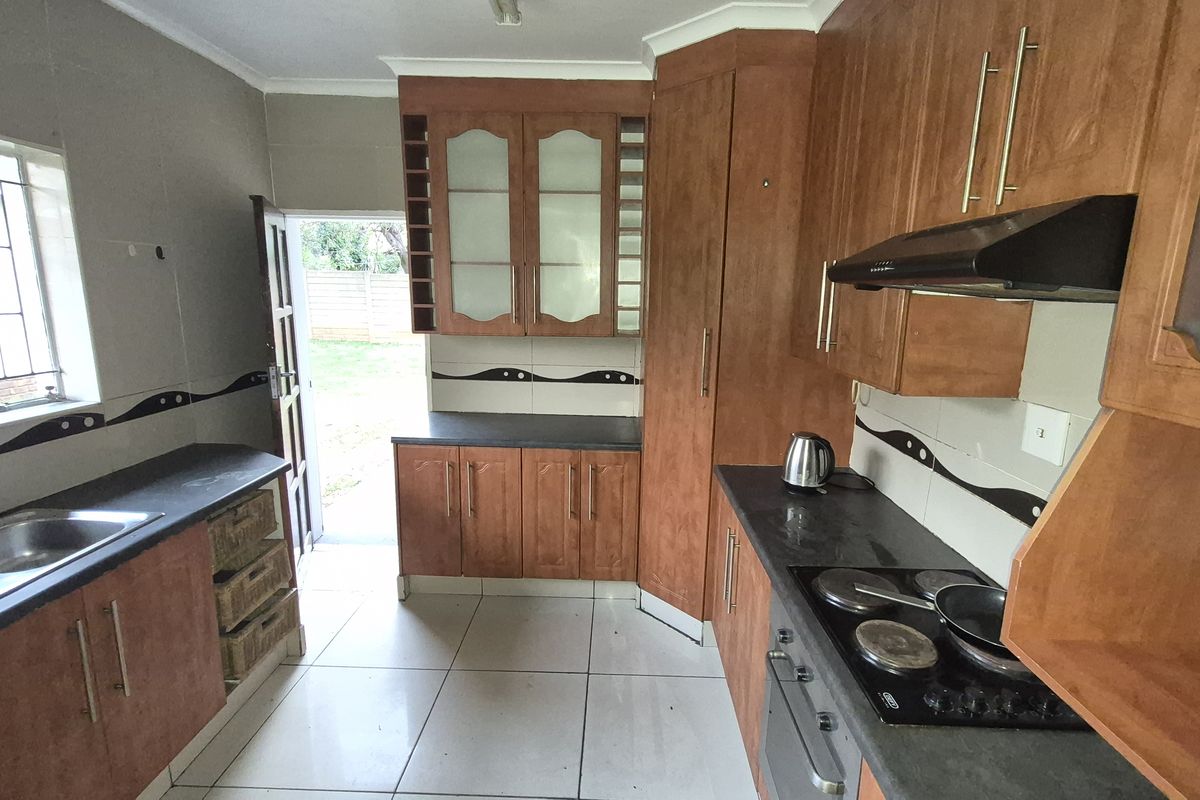 A functional kitchen featuring wooden cabinetry, dark countertops, a built-in oven with hob, and tiled flooring with direct access to the rear garden.