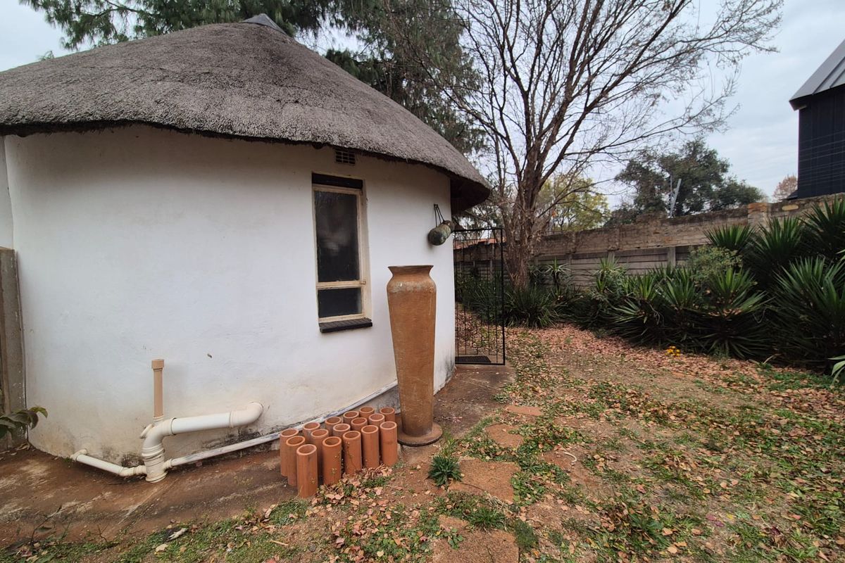 Exterior view of a circular structure with a traditional thatched roof, featuring exposed plumbing and a surrounding garden area.