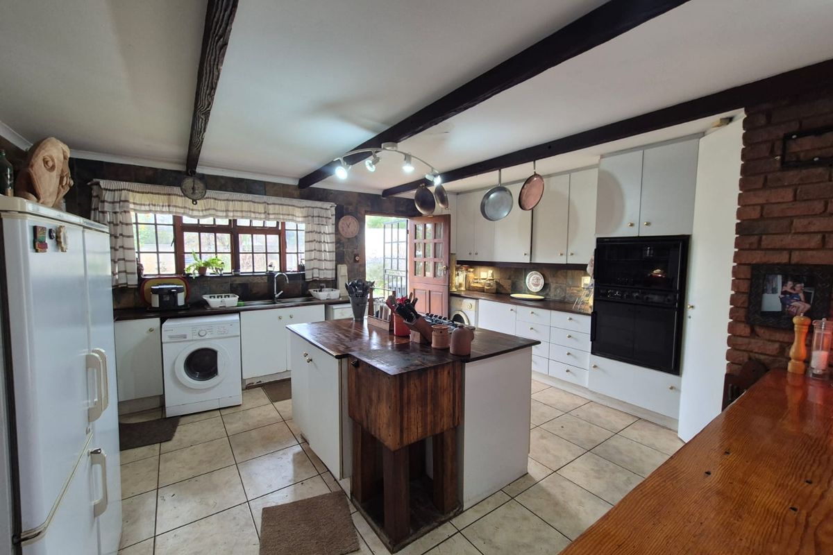 A rustic kitchen featuring a central island with a wooden butcher block top, built-in oven, and tiled flooring with exposed ceiling beams.