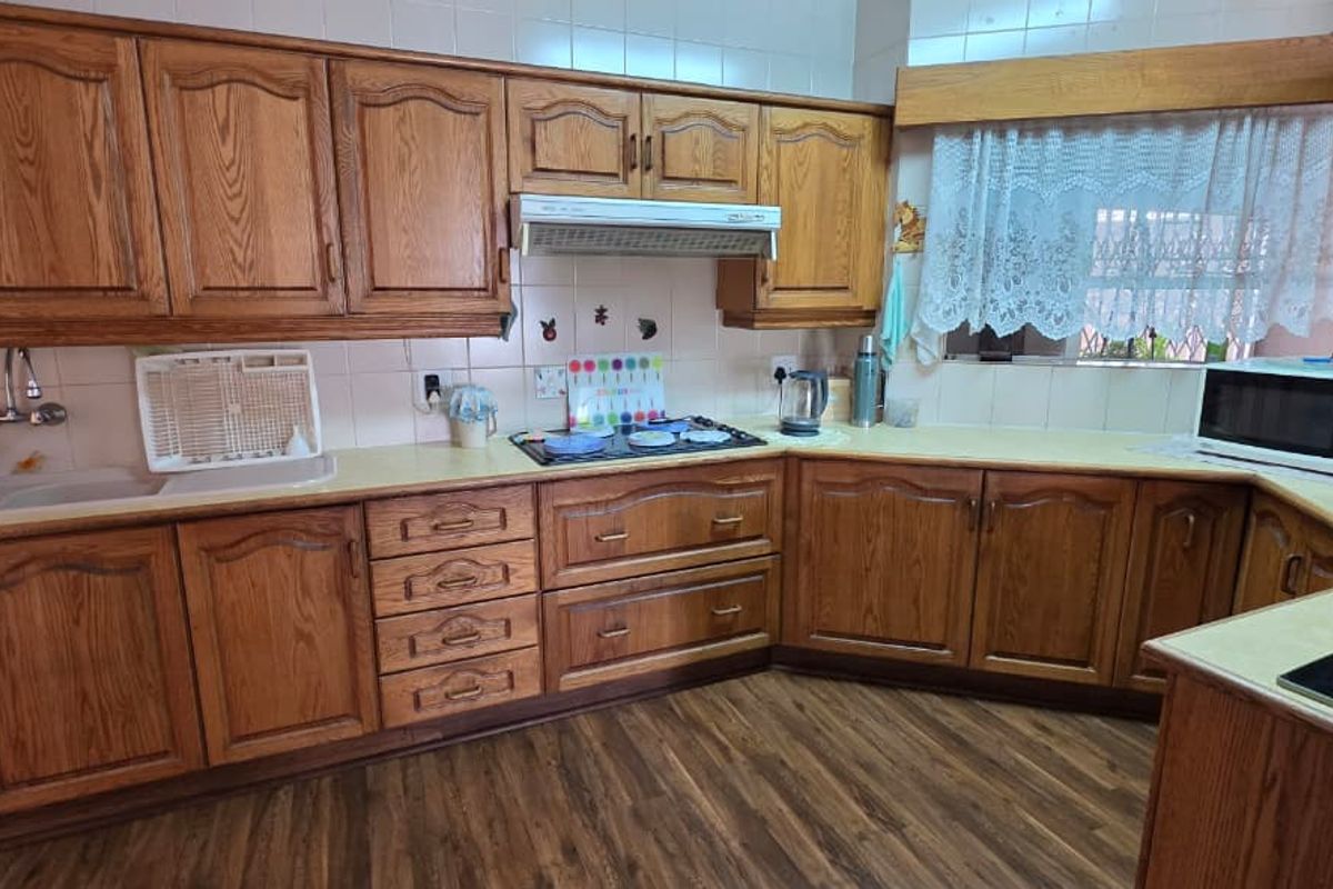A functional kitchen featuring traditional timber cabinetry, a built-in extractor fan, a gas hob, and ample laminate countertop workspace.