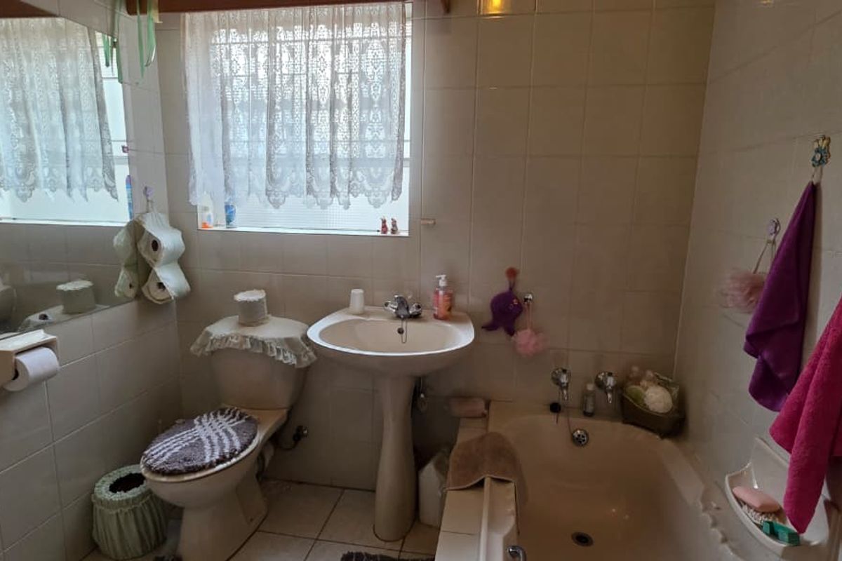 A dated bathroom featuring a pedestal basin, a built-in bathtub, and full-height wall tiling with a window for natural light.
