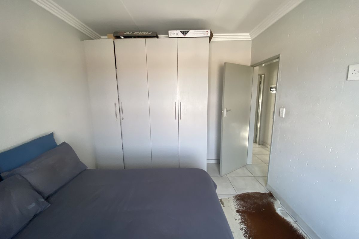 A bedroom featuring built-in cupboards, tiled flooring, and direct access to an adjoining hallway.