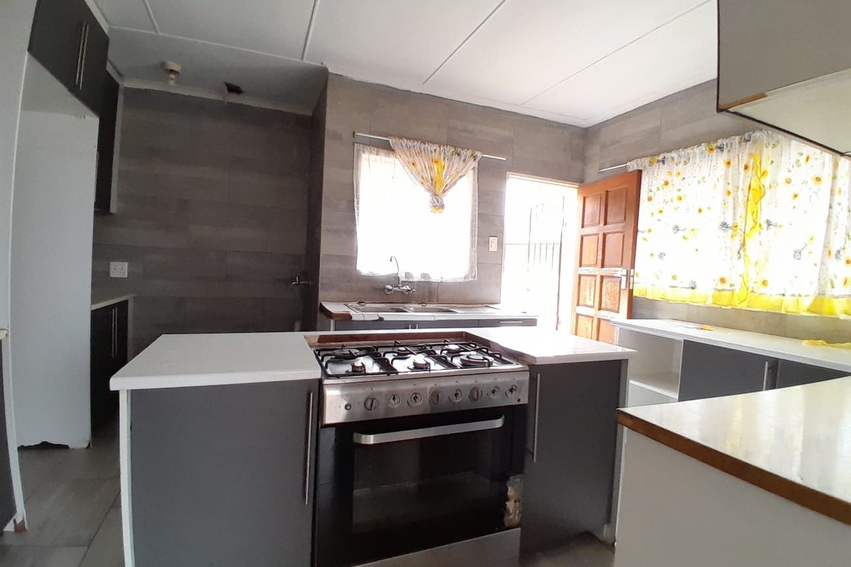 A functional kitchen featuring a central island with a built-in gas stove, grey cabinetry, tiled walls, and direct access to the exterior.